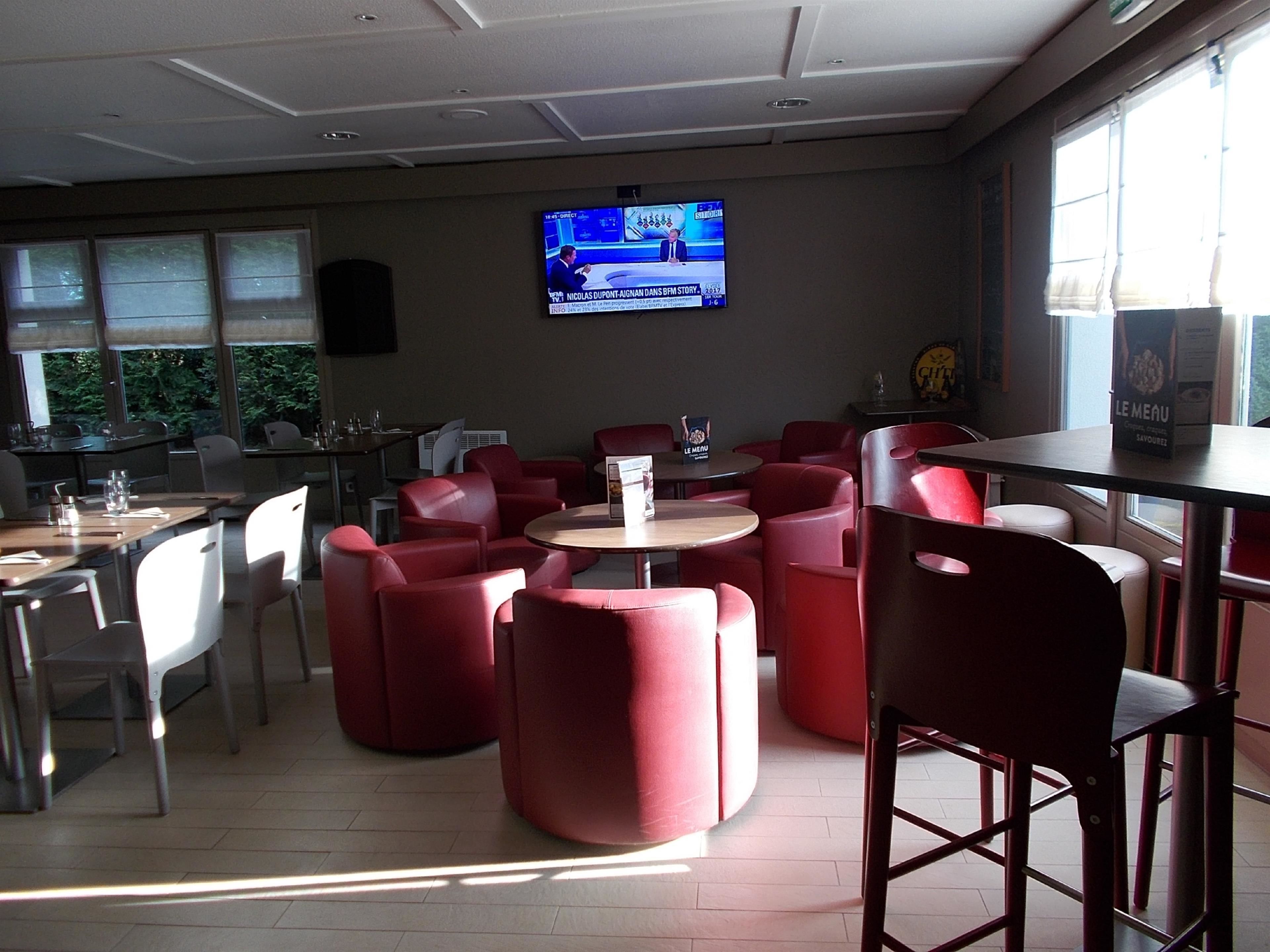 A restaurant with red upholstered chairs, a TV mounted on the wall, and a menu stand.
