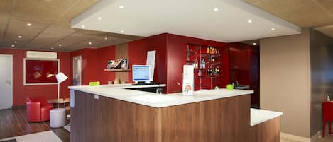 A modern reception area with a wooden counter, a computer, and a red wall with shelves.