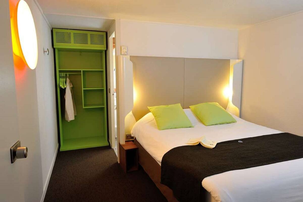 Une chambre d’hôtel avec un lit, des lampes de chevet, une armoire verte et un miroir.