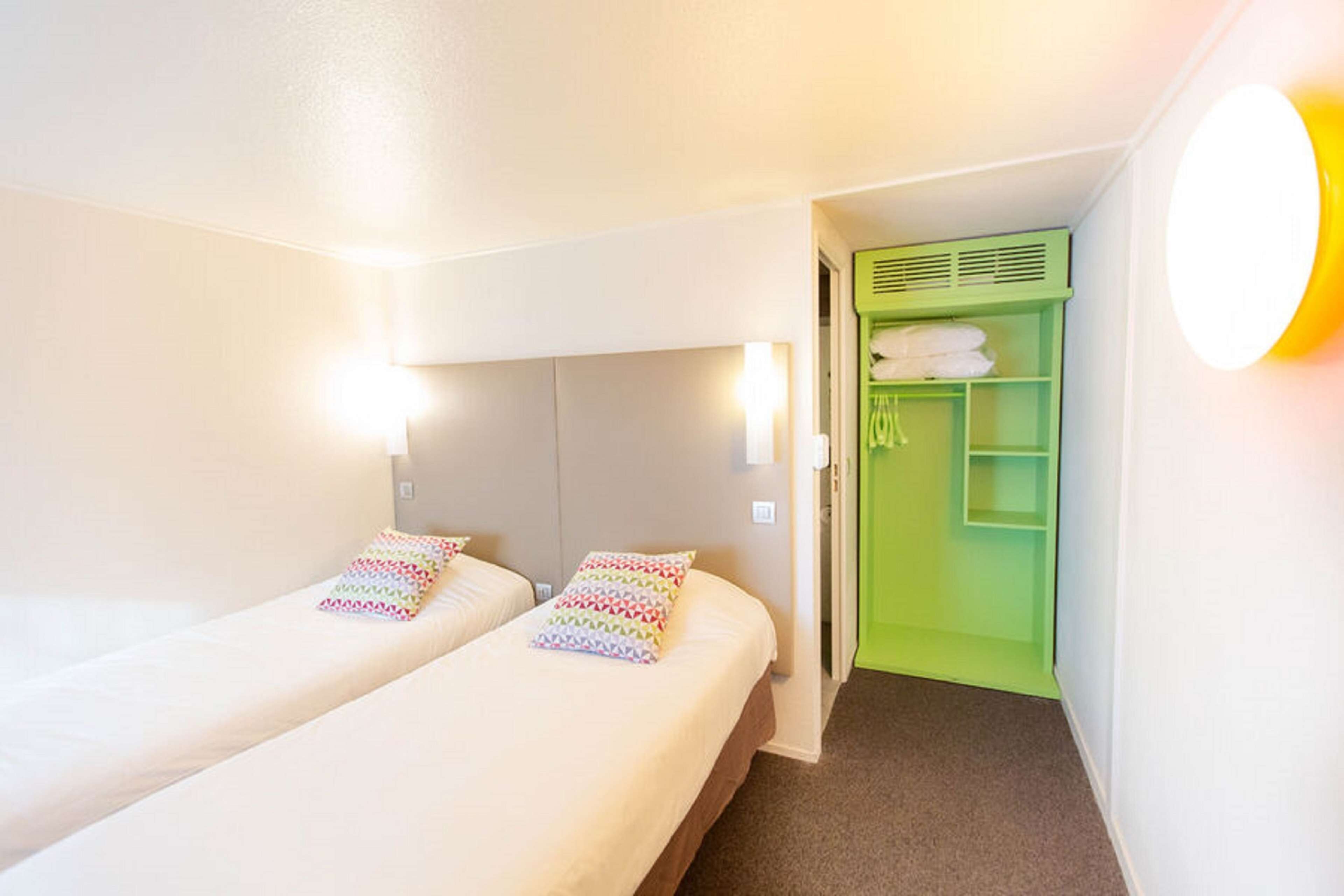 A hotel room with two beds, a green wardrobe, and a light fixture.
