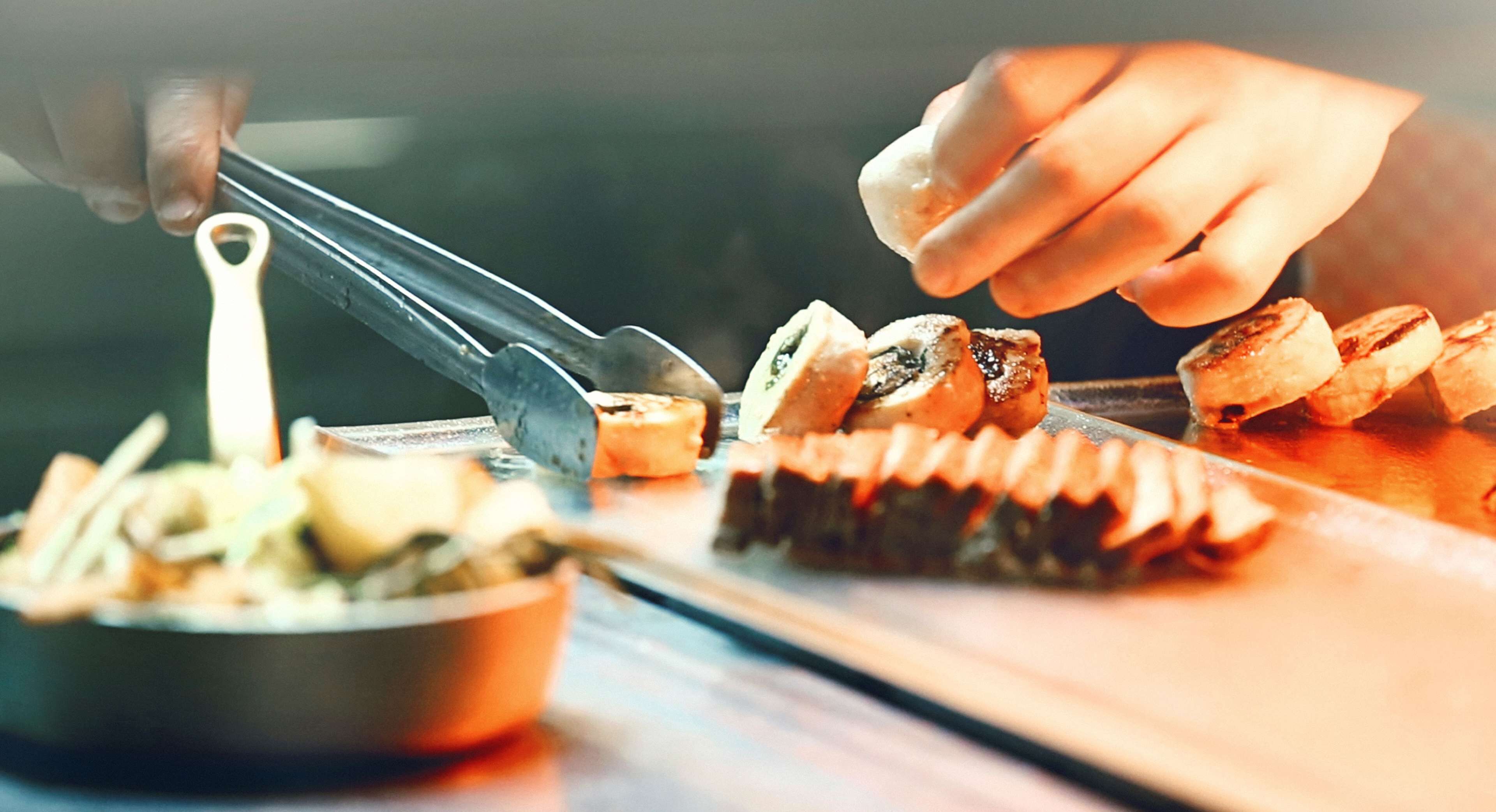 A hand using tongs to handle food on a cutting board.