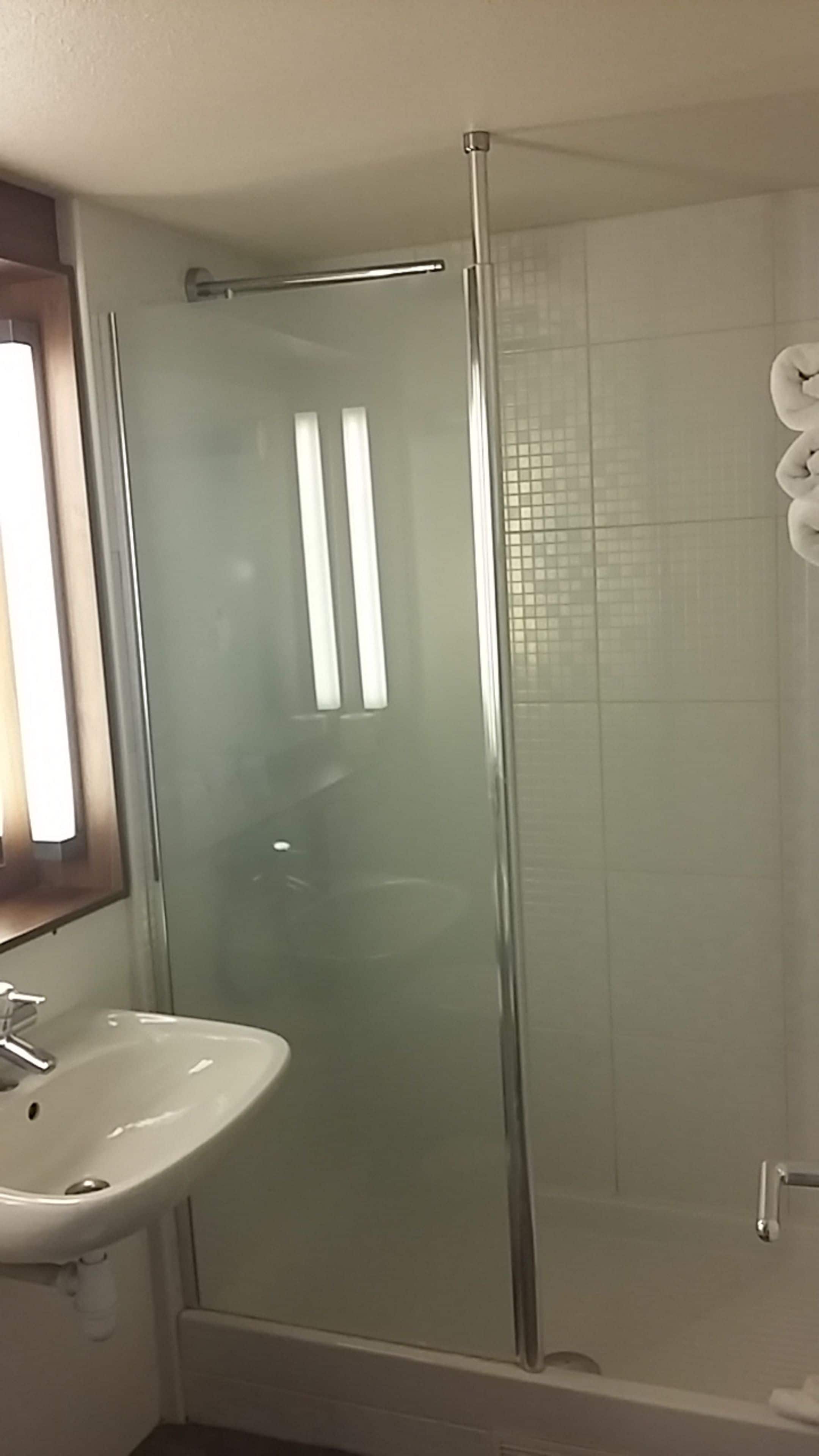 Een badkamer met een douchecabine van glas, een wit wastafelmeubel en een spiegel boven het badkamermeubel.