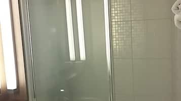 Een badkamer met een douchecabine van glas, een wit wastafelmeubel en een spiegel boven het badkamermeubel.