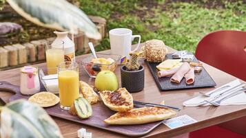 Una mesa de desayuno con diferentes alimentos, una jarra, un vaso de zumo de naranja y una taza.