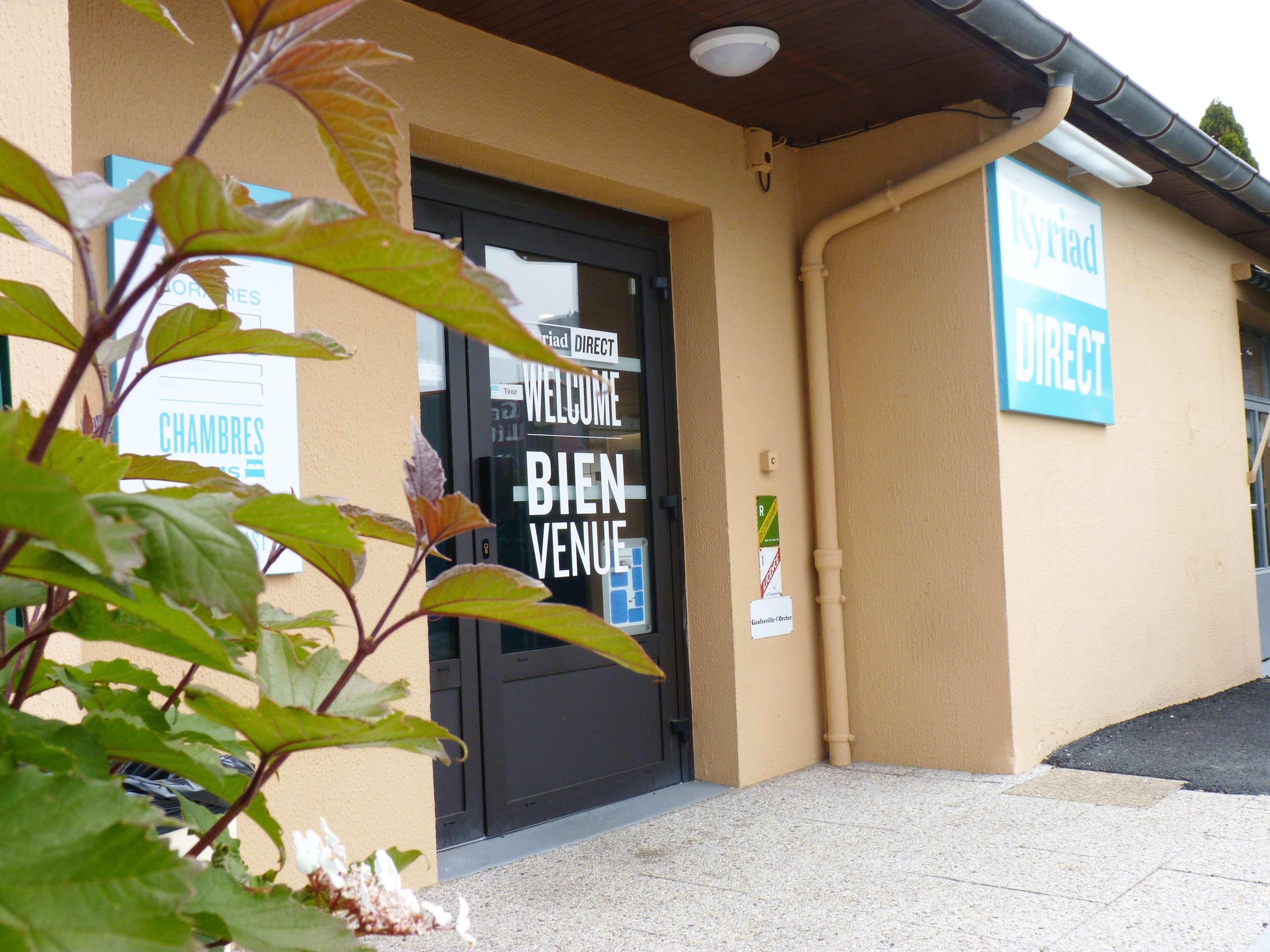 A building entrance with a black door, a sign reading "WELCOME BIENVENUE", and another sign "Kyria Direct".