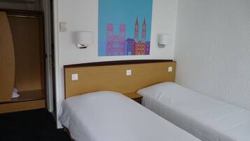 Una habitación de hotel con dos camas individuales, cabecero de madera, aire acondicionado montado en la pared y un cuadro de un paisaje urbano colorido sobre las camas.