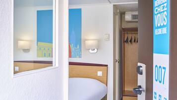 A hotel room with a bed, a wardrobe, and a door with a number sign.