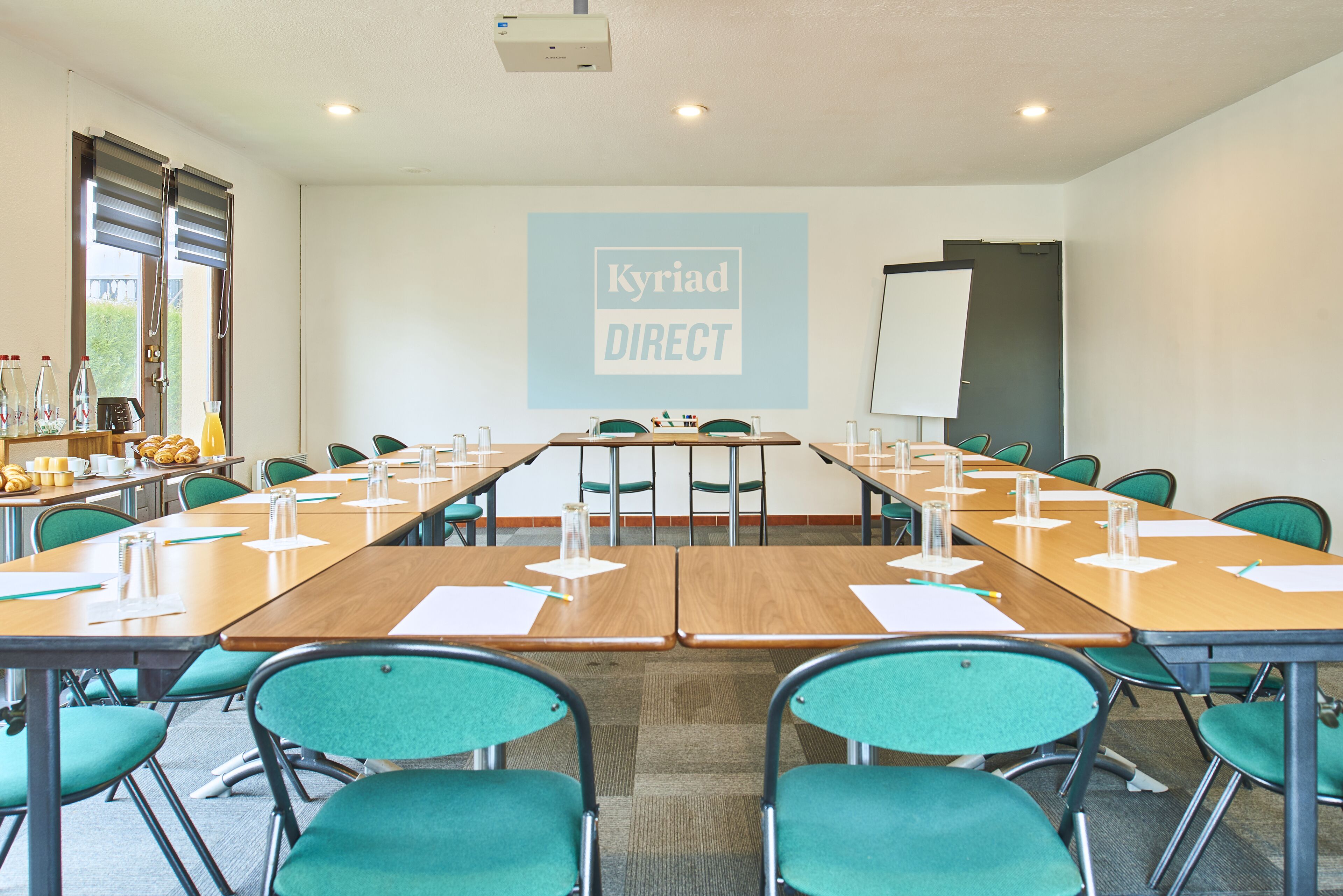 A conference room with long tables, green chairs, and a whiteboard with 'Kyriad DIRECT' written on it.