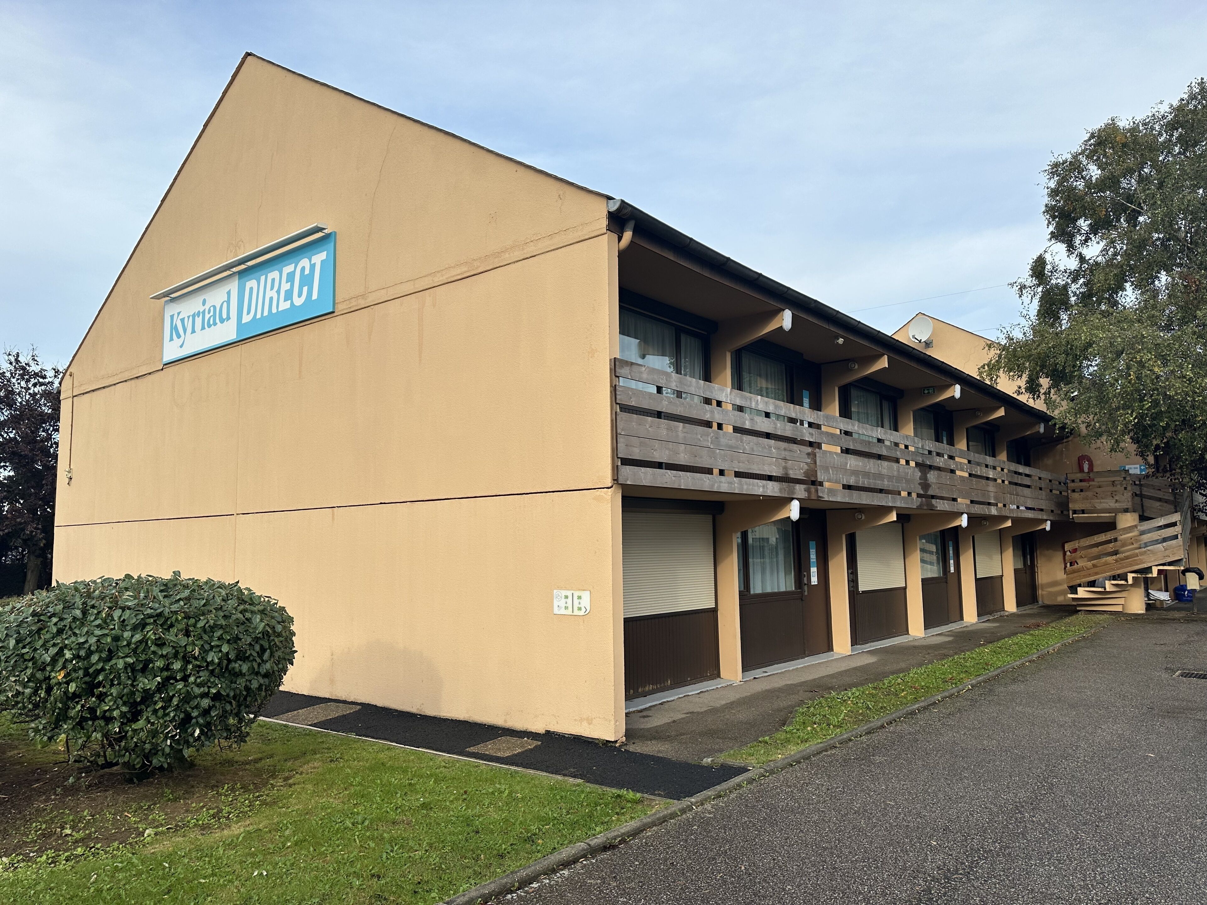 A building with a sign reading "Kyriad Direct" and a wooden balcony.