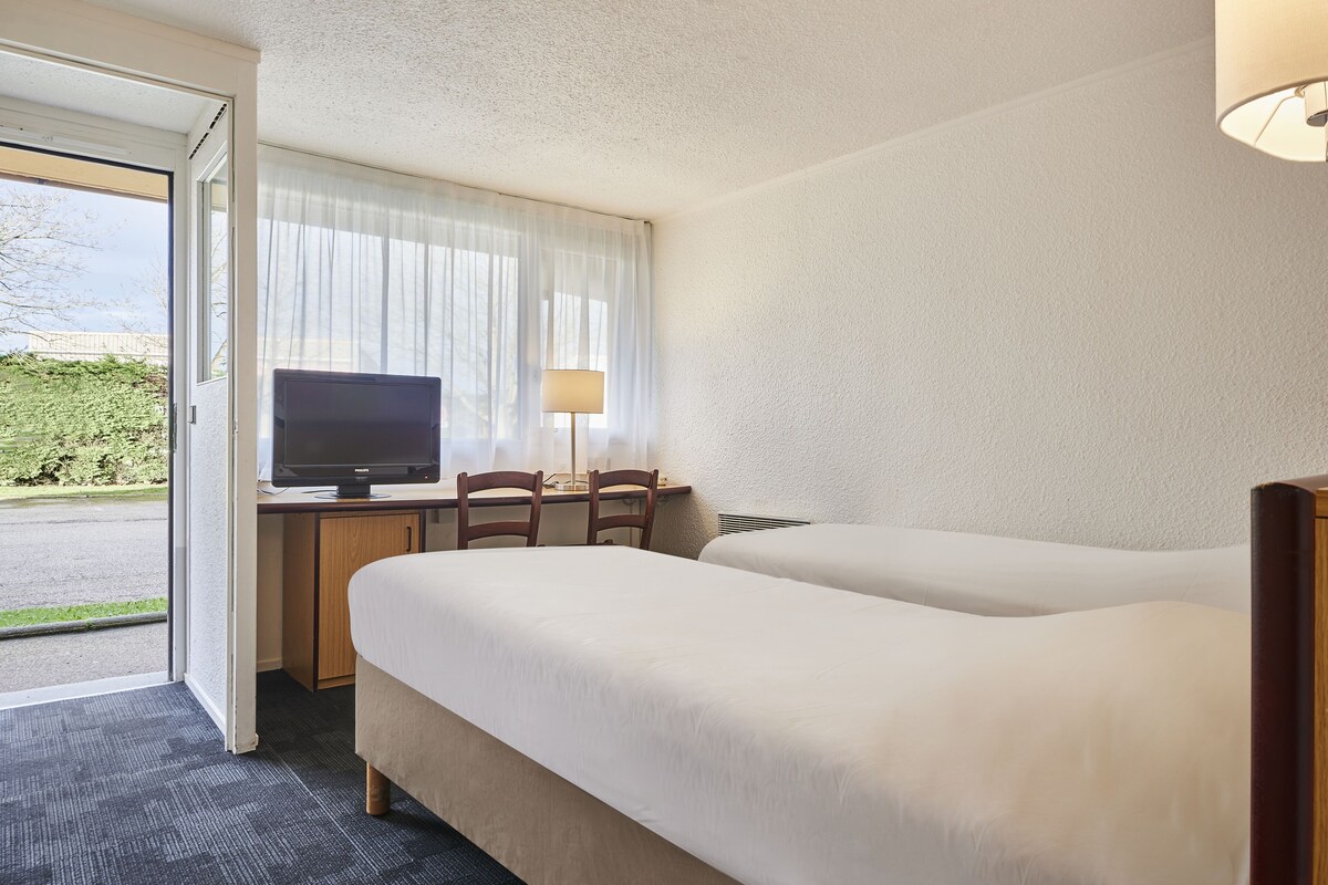 Une chambre d’hôtel avec deux lits, un bureau équipé d’un ordinateur, une lampe et un téléviseur.