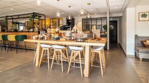 A modern bar area with a wooden bar counter, multiple stools, and a variety of bottles and jars. - Campanile NATURE - Limoges Nord (Limoges)