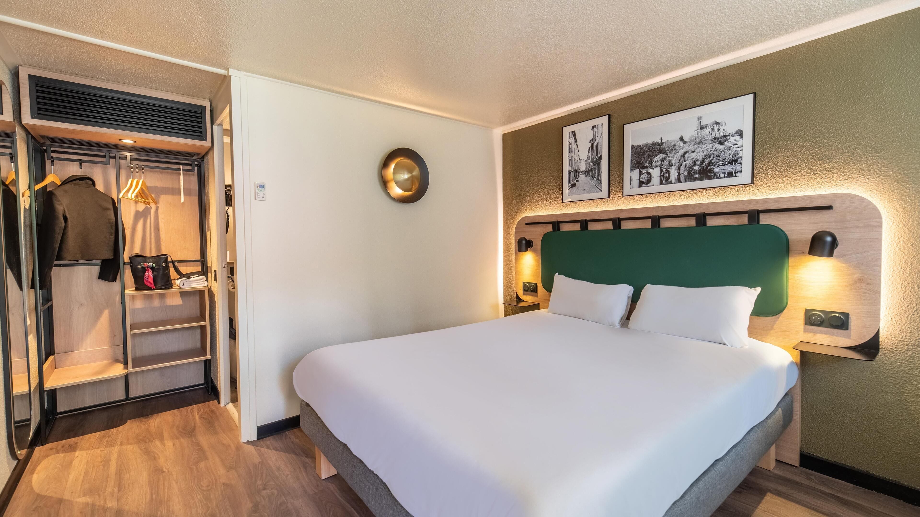 A hotel room with a large bed, a wardrobe, and a wall-mounted lamp.