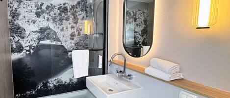 A modern bathroom with a glass shower, a white sink, a mirror, and a towel rack.
