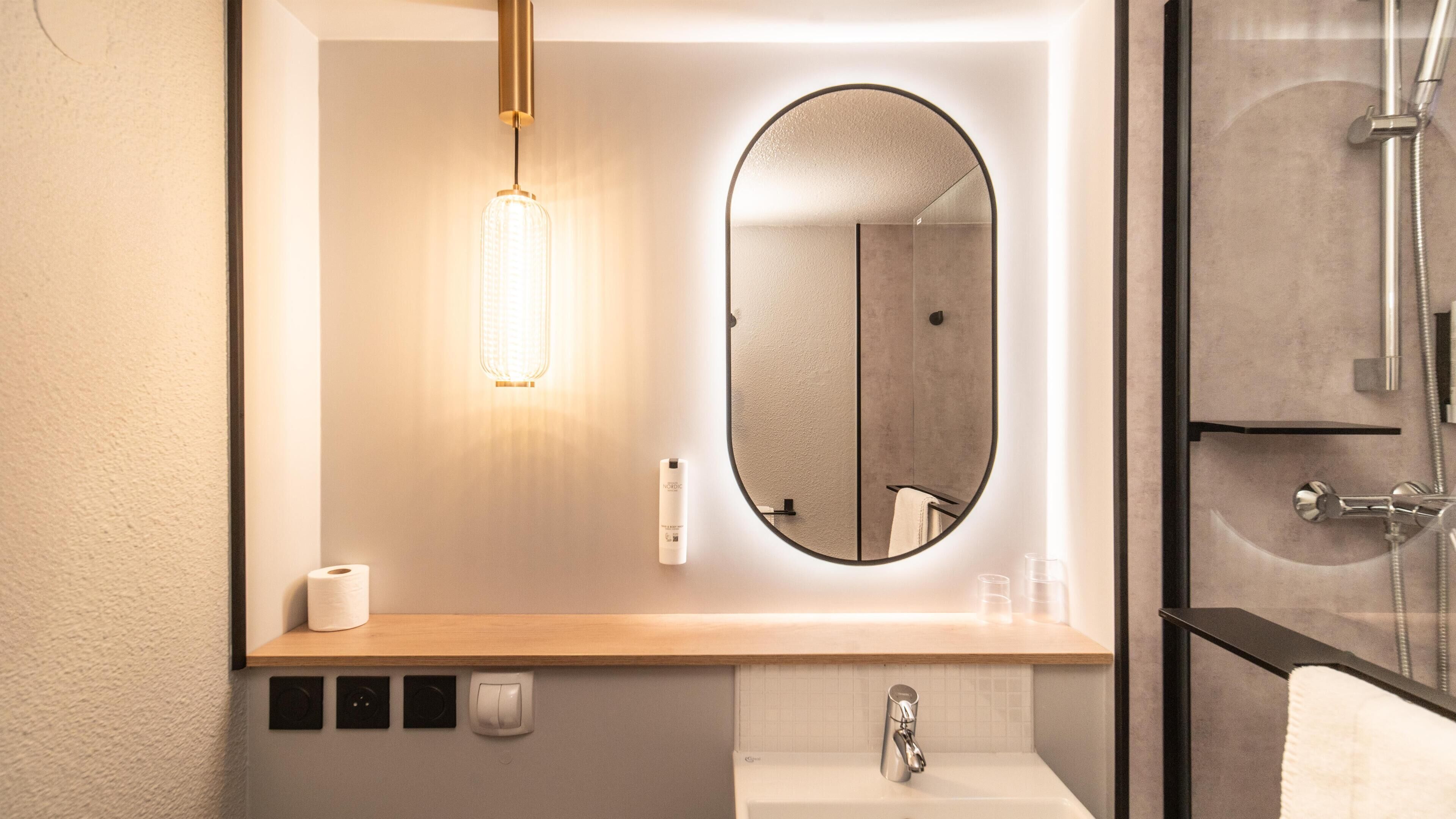 Un baño moderno con tocador de madera, espejo redondo, cabina de ducha de cristal y lámpara colgante.