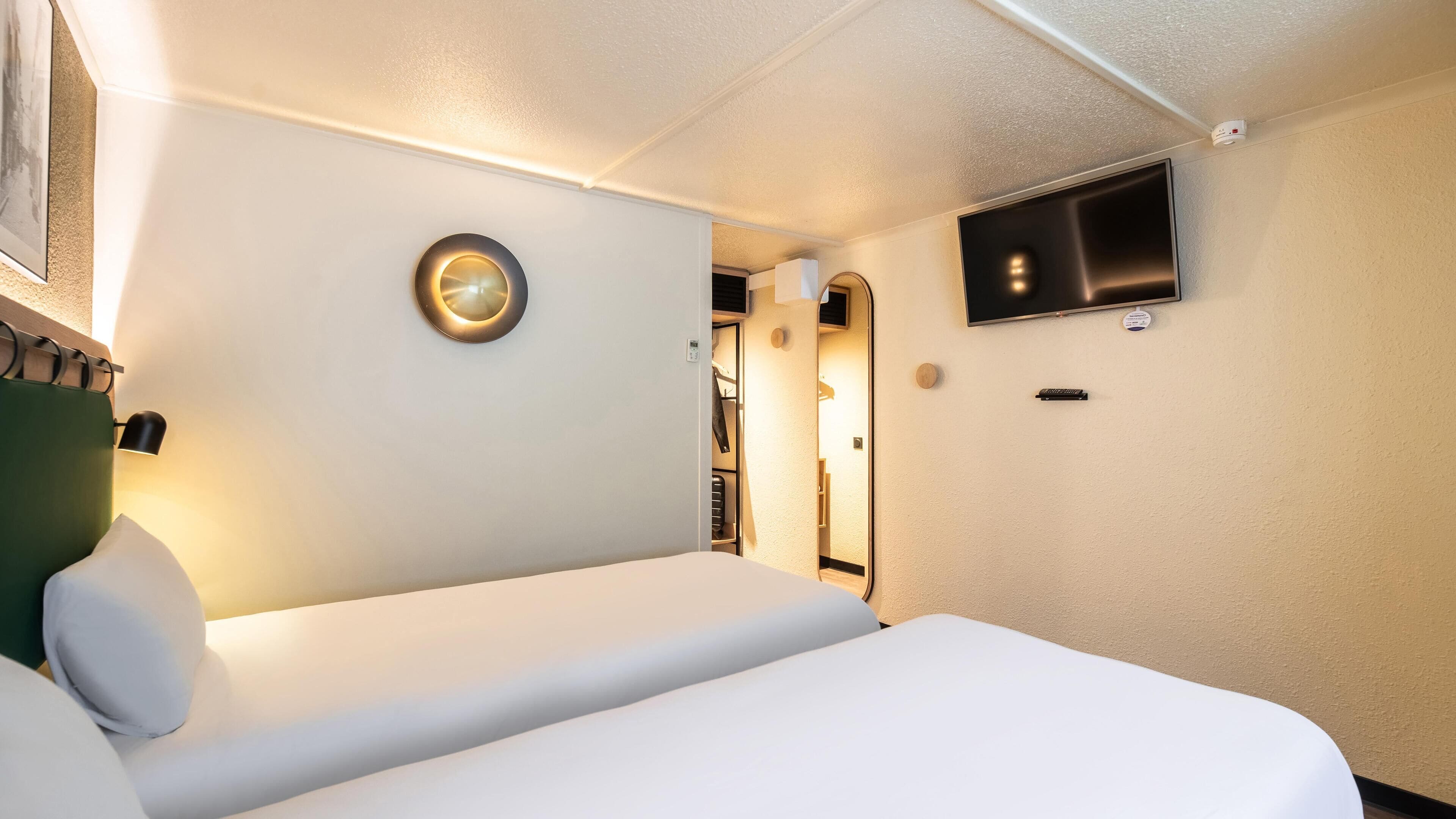 A hotel room with a bed, a wall-mounted TV, and a circular light fixture.