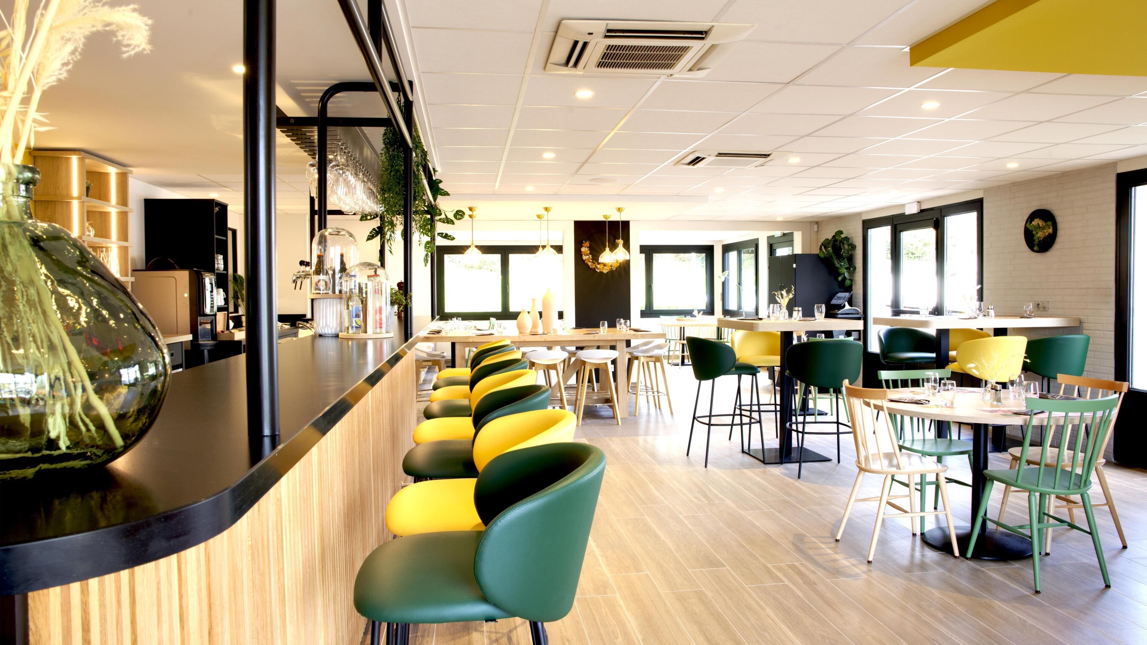 A modern restaurant with a bar area, green and yellow chairs, and a wooden counter.
