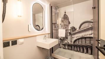 A bathroom with a large mirror, a sink, and a glass shower enclosure.
