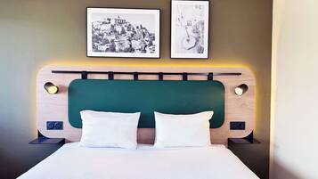A neatly made bed with a green upholstered headboard, two white pillows, and two bedside lamps. Above the bed, there are two framed black-and-white photographs on the wall.