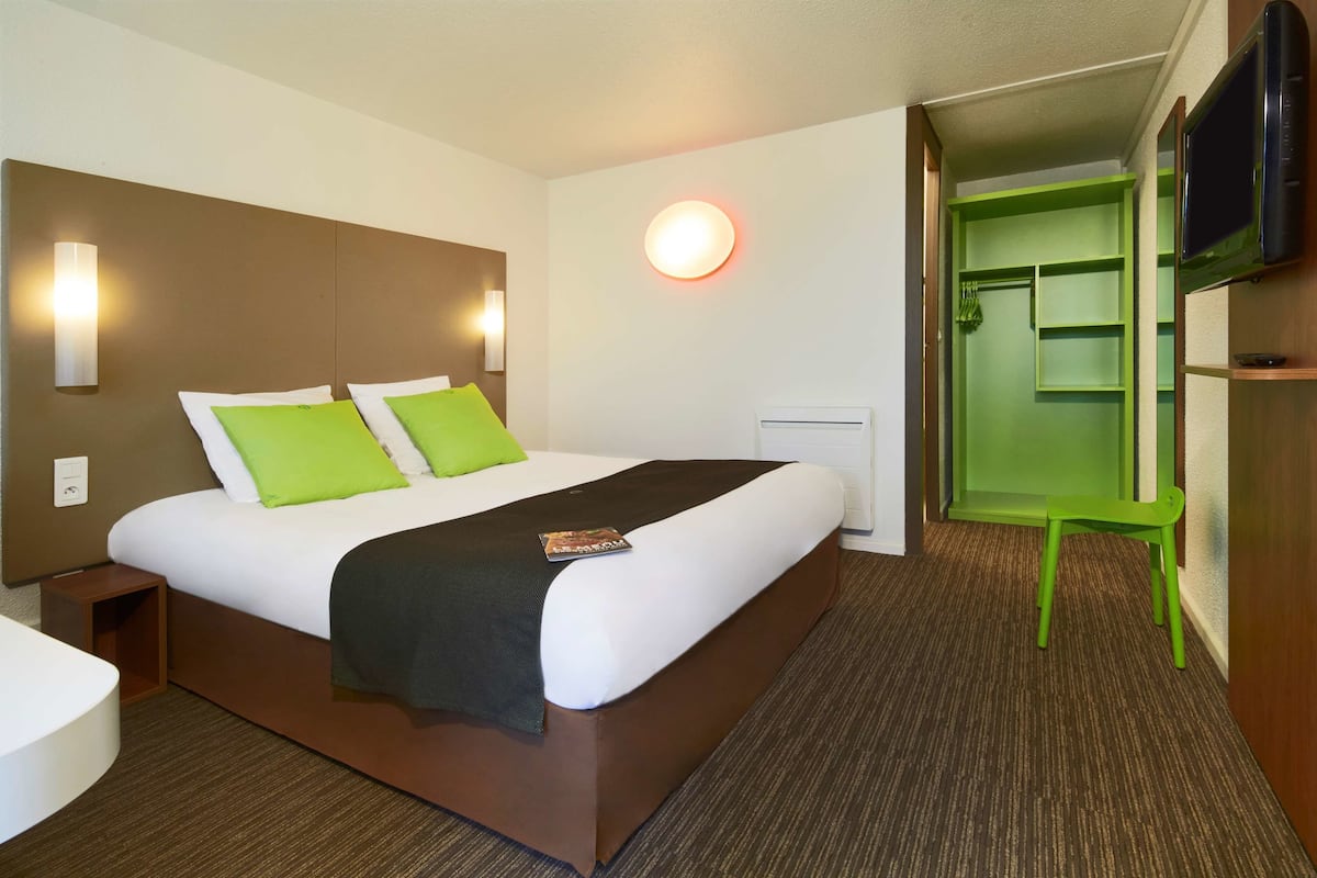 Ein Hotelzimmer mit einem großen Bett, grünen Kissen, einem Nachttisch, einem Flachbildfernseher und einem grünen Sessel.