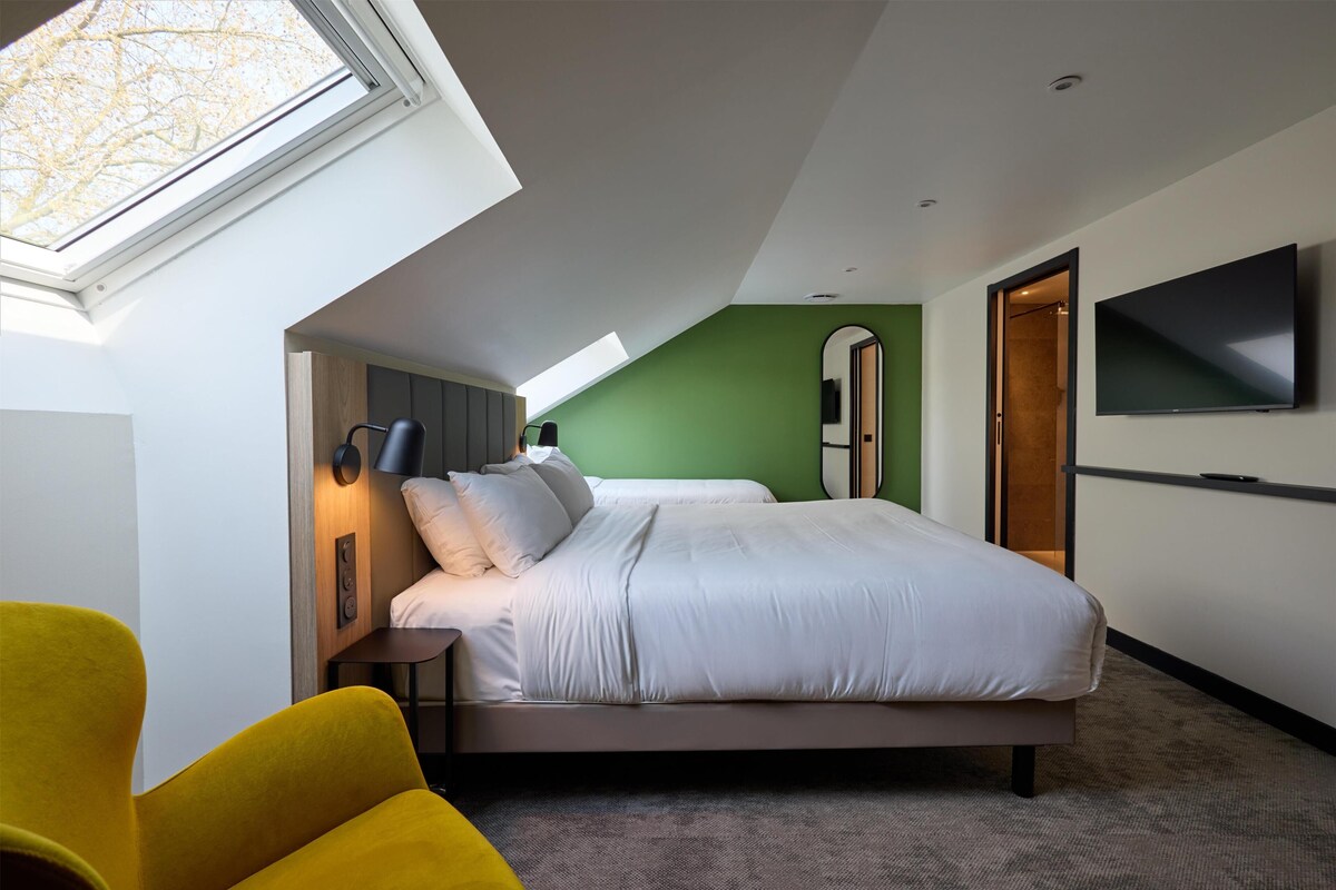 Ein modernes Schlafzimmer mit Dachfenster, einem Bett, einem Fernseher und einem gelben Sessel.