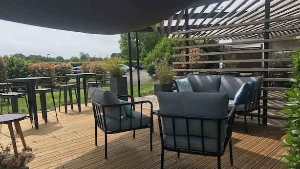 Un patio al aire libre con piso de madera, sillas y mesas de metal negro.