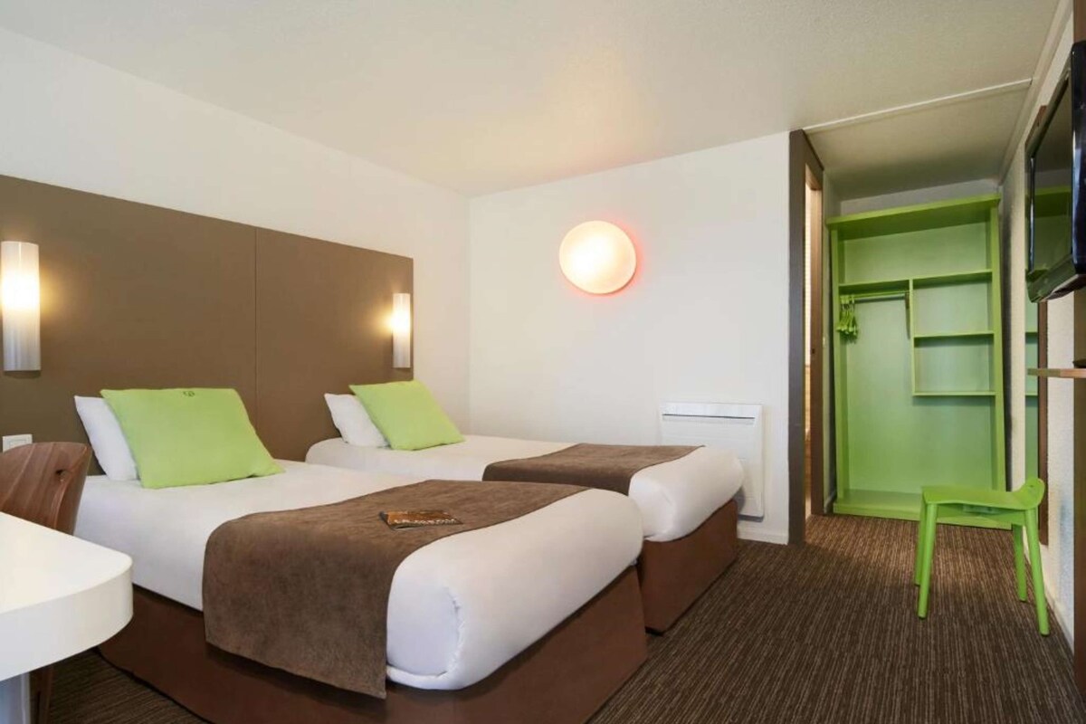Ein Hotelzimmer mit zwei Betten, einem Schreibtisch und einem grünen Stuhl.
