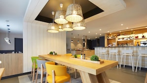 Un restaurante moderno con barra de madera, sillas amarillas y lámparas de mimbre colgantes.