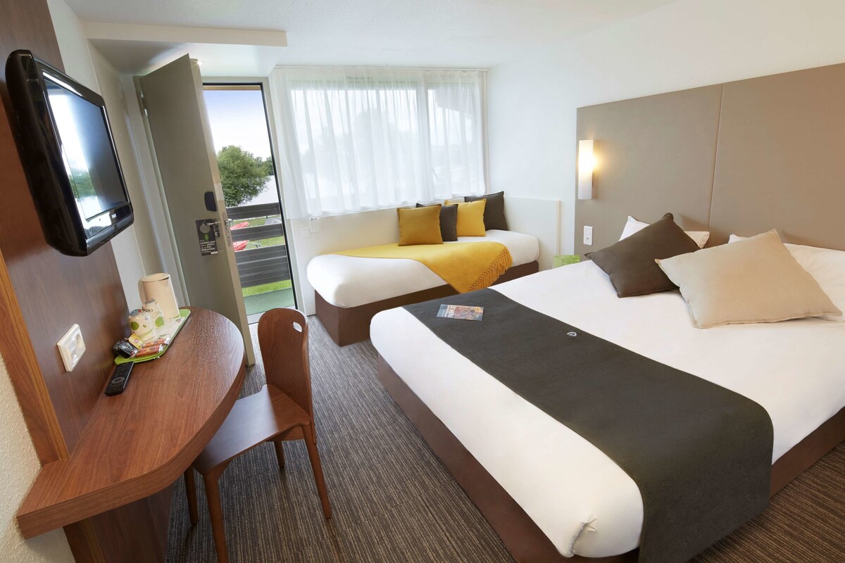 Ein Hotelzimmer mit einem Bett, einem Schreibtisch mit Stuhl, einem Fernseher und einem Fenster mit Vorhängen.