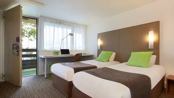 Habitación de hotel con dos camas, un escritorio con una computadora portátil, una silla y una puerta que da a un balcón.