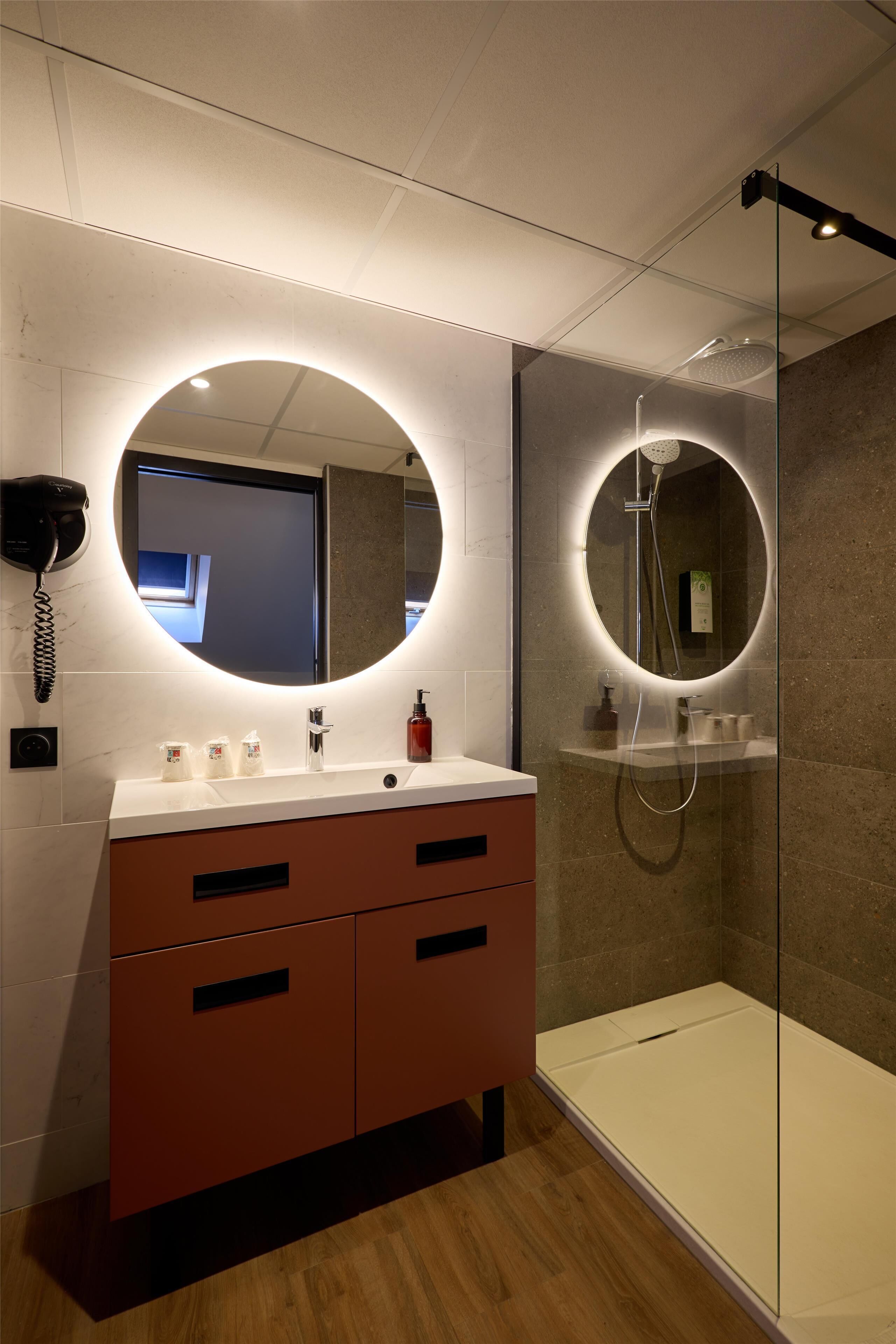 Een moderne badkamer met een ronde spiegel, een douchecabine van glas en een houten vloer.