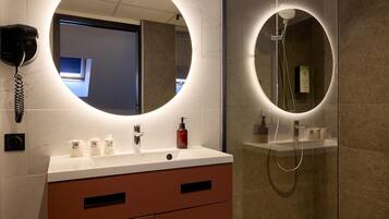 Een moderne badkamer met een ronde spiegel, een douchecabine van glas en een houten vloer.