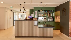 Een receptie met een houten balie, hangende lampen, een digitaal scherm en een bar voorzien van flessen.