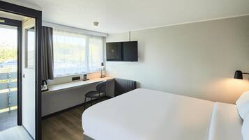 Une chambre d’hôtel équipée d’un lit, d’un bureau, d’une chaise, d’une télévision et d’une fenêtre avec des rideaux.