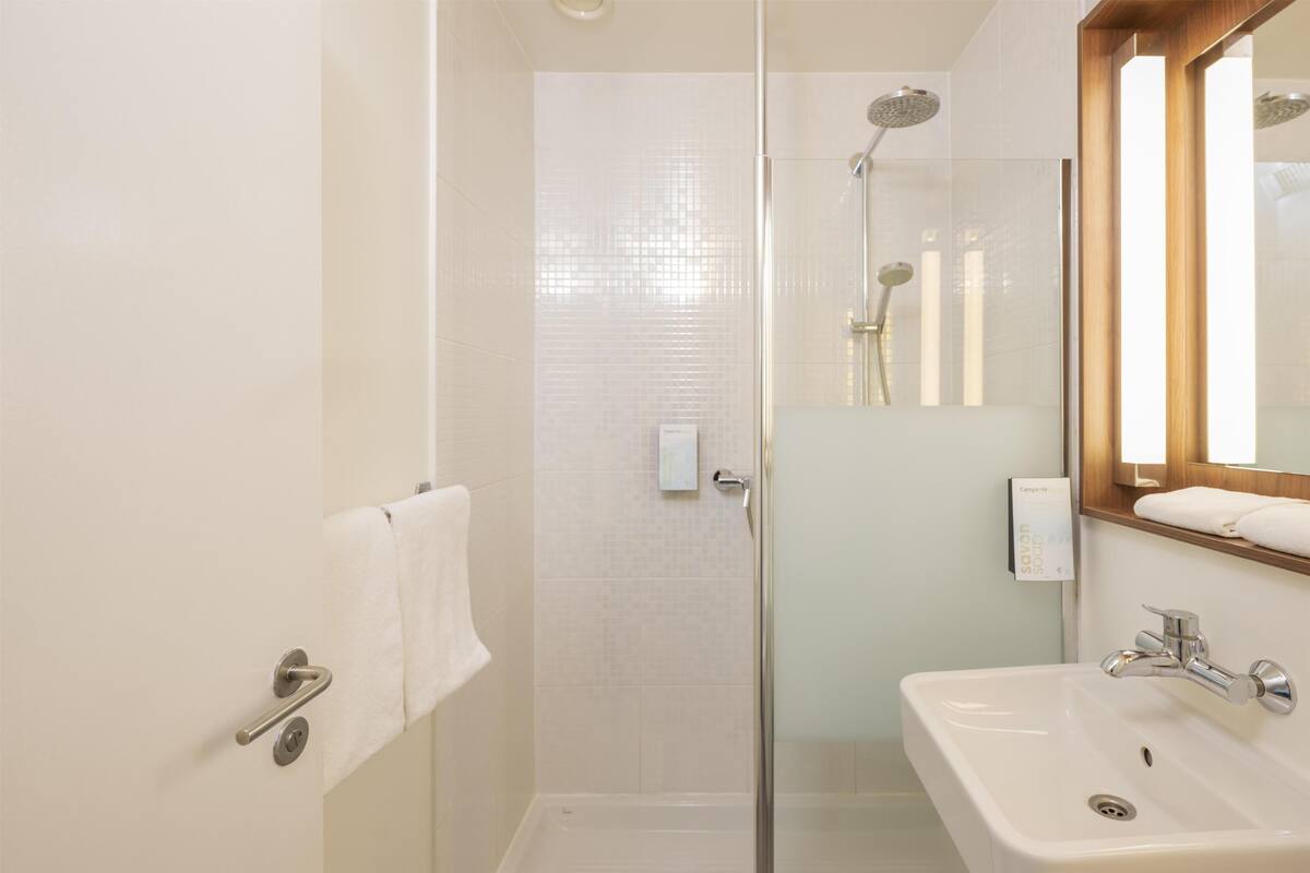 A bathroom with a glass-enclosed shower, a sink, and a mirror.