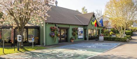 Un edificio con fachada verde, una zona de estacionamiento para bicicletas y una bandera.
