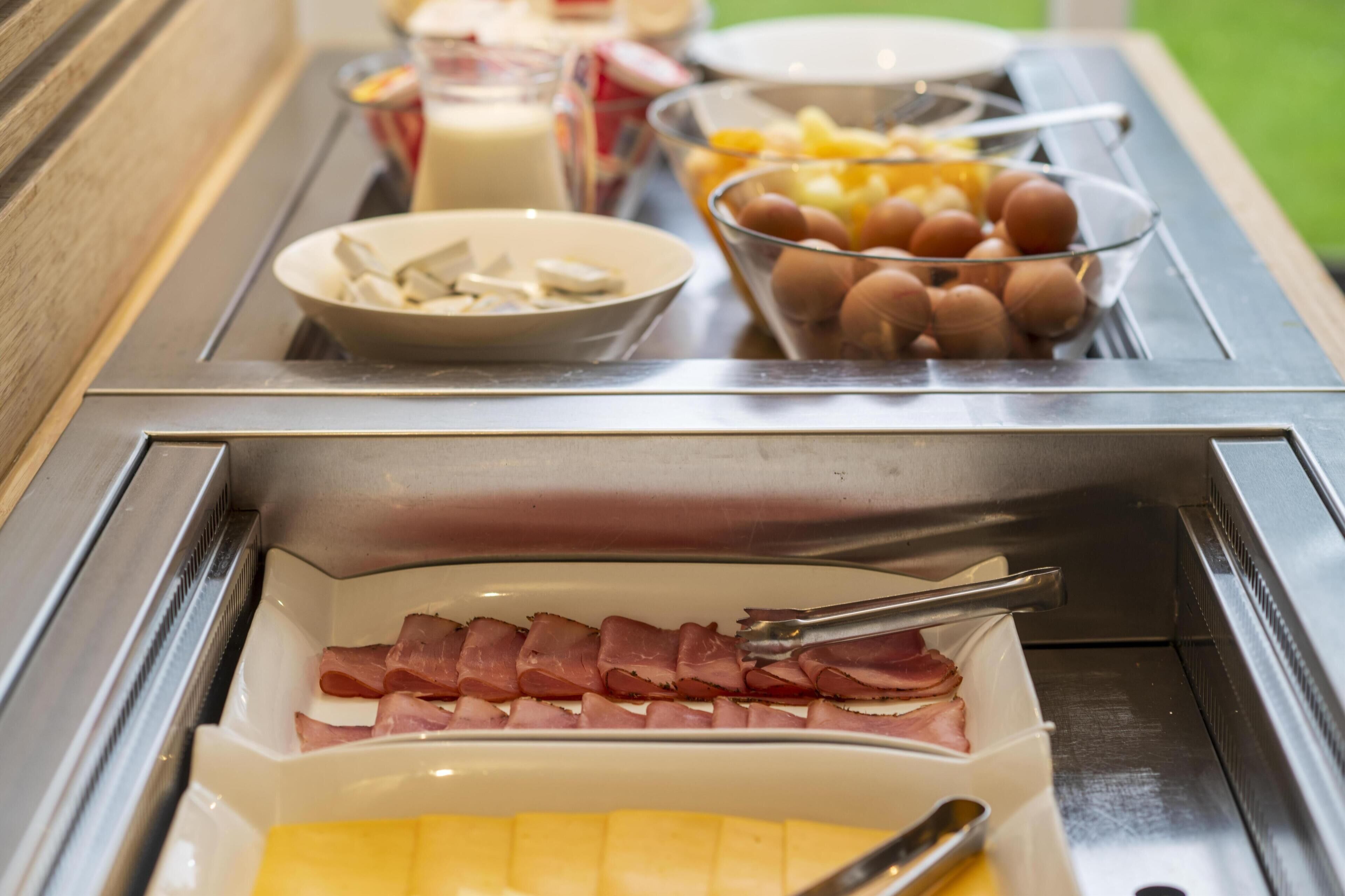 Een ontbijtbuffet met ham, kaas, eieren en fruit.