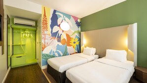 Habitación de hotel con dos camas, un armario verde, un mural colorido y un equipo de aire acondicionado.