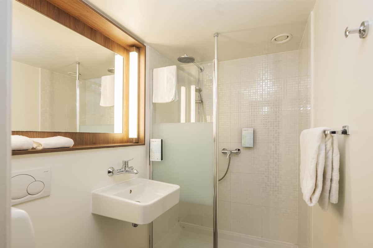 A modern bathroom with a glass-enclosed shower, a white sink, and a mirror with a wooden frame.