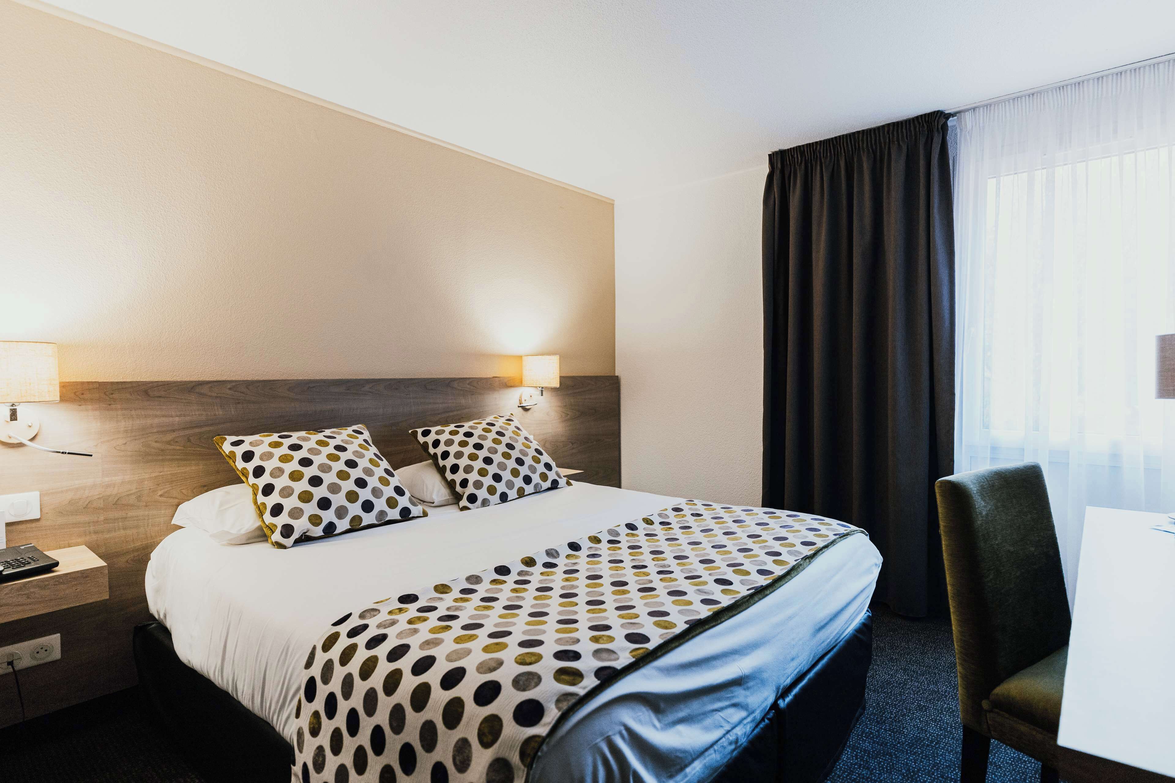 A hotel room with a bed, two bedside lamps, a desk, and a chair.