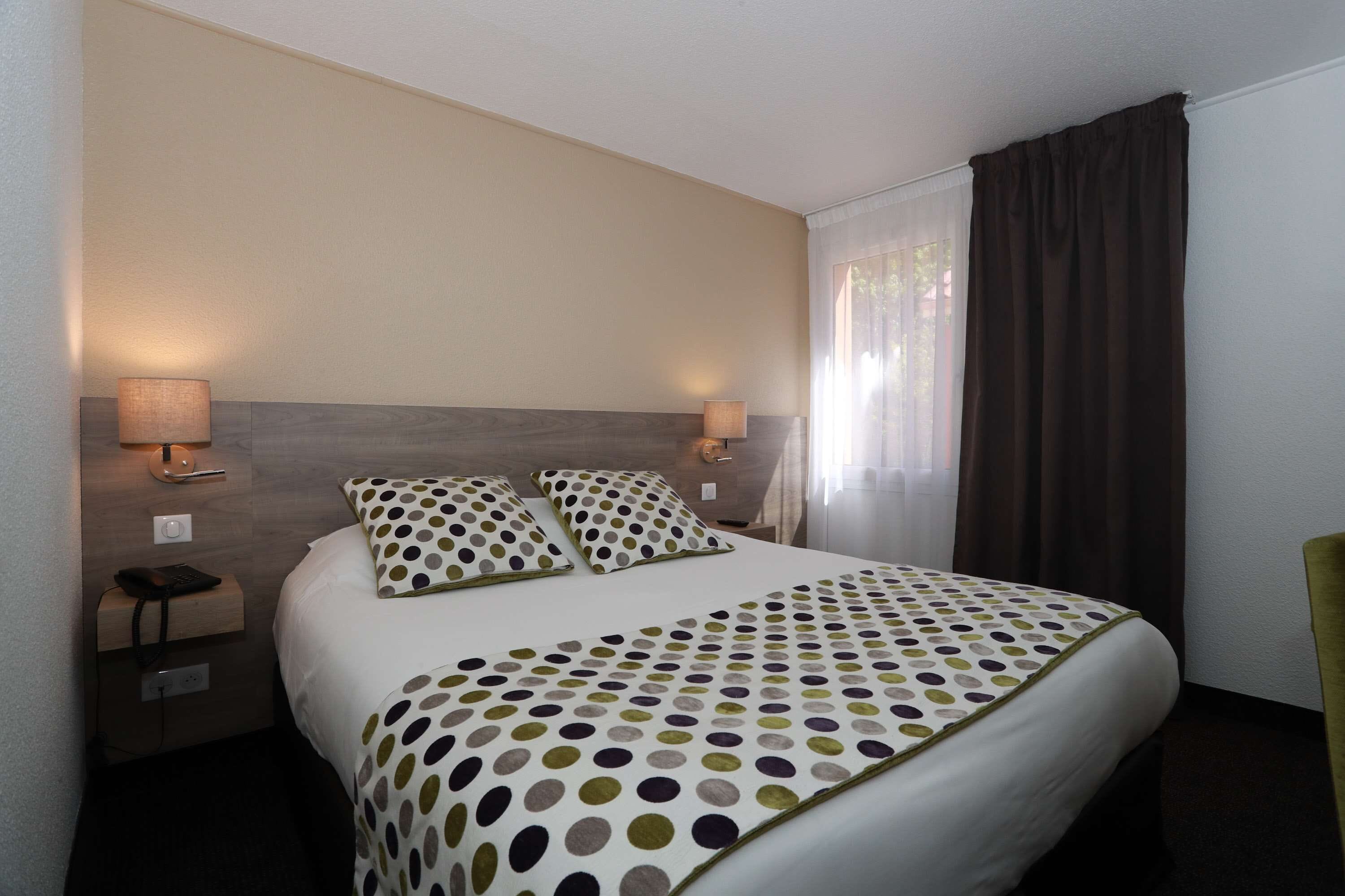A hotel room with a large bed, two bedside lamps, a nightstand with a phone, and a window with curtains.