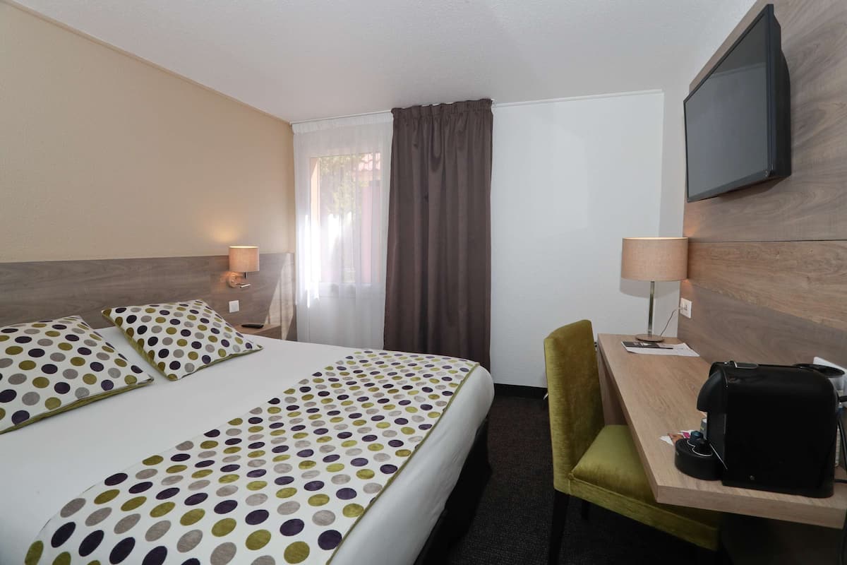 A hotel room with a bed, a desk, a chair, a TV, and a window with curtains.