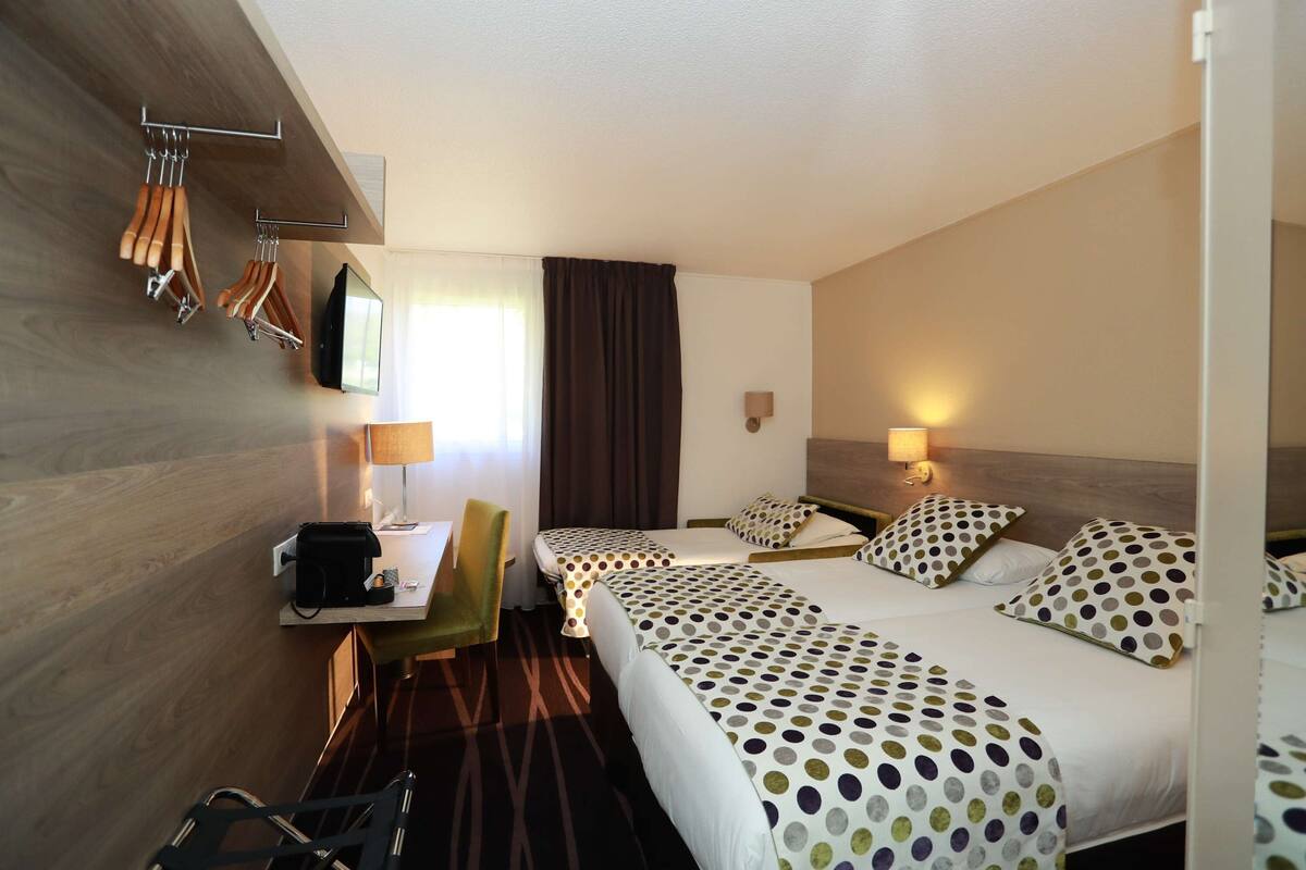 A hotel room with two beds, a desk with a chair, a TV, and a coat rack.