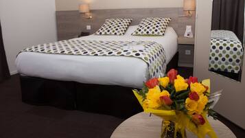 Una habitación de hotel con cama, lámparas de noche, un espejo y un jarrón con flores.