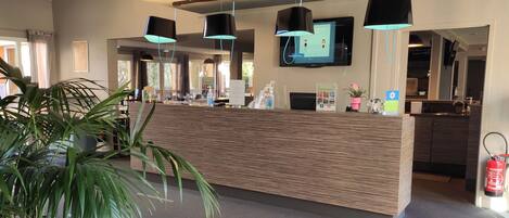 A modern reception area with a wooden reception desk, black pendant lights, a flat-screen TV, and a potted plant.