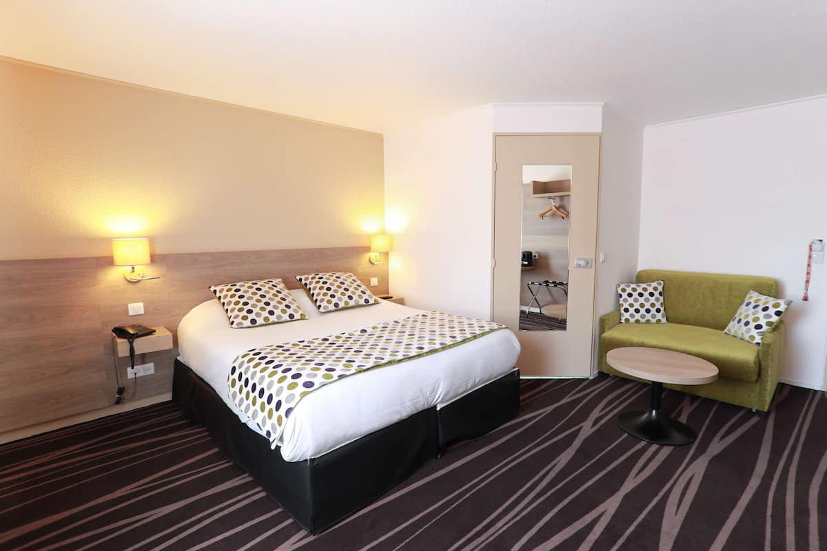 A hotel room with a bed, a green armchair, a small round table, and two bedside lamps.