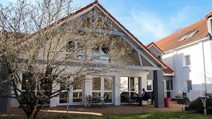 A modern house with a covered patio, a tree in the foreground, and a clear sky.
