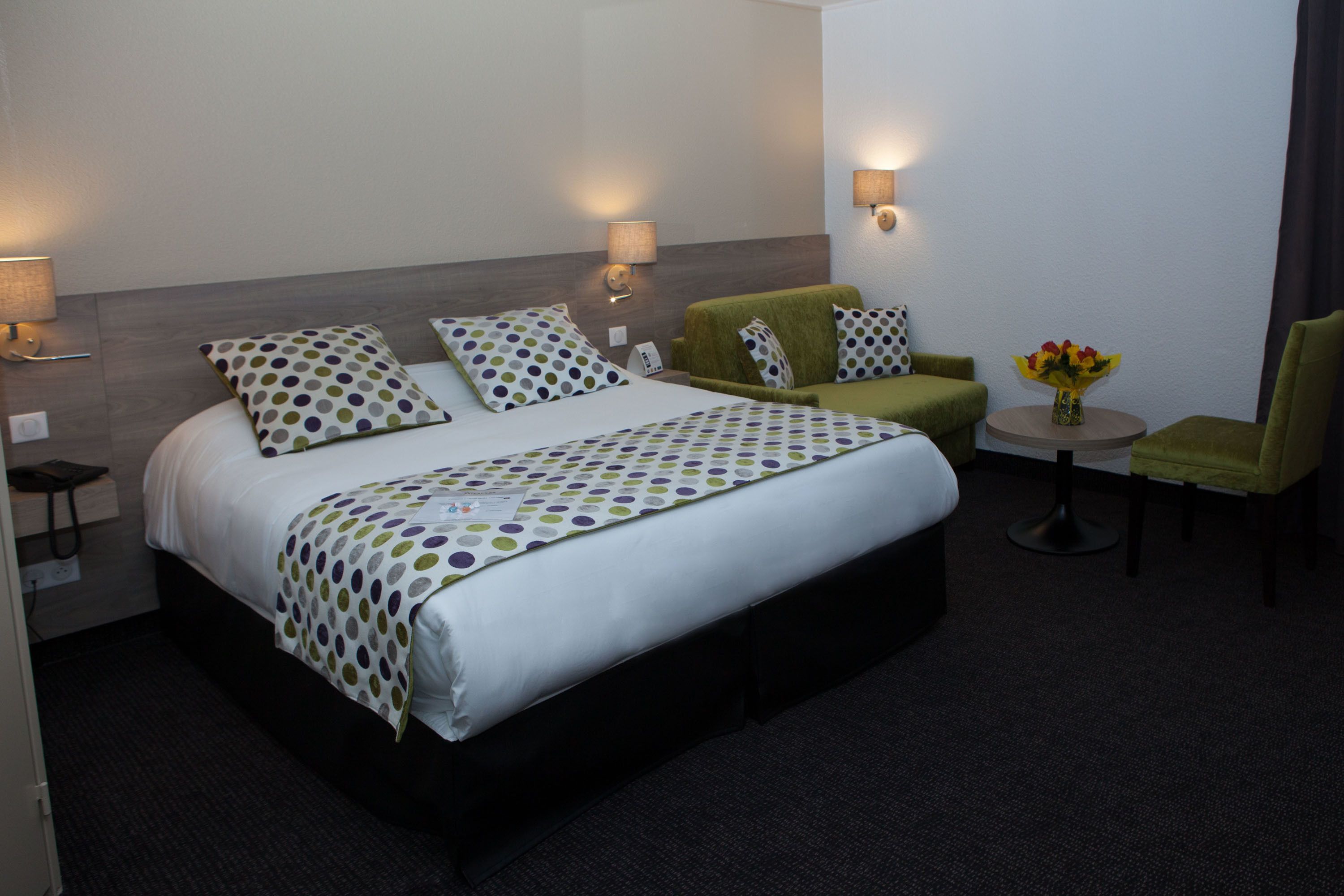 A hotel room with a large bed, two bedside tables, a chair, a small table with a vase of flowers, and two wall-mounted lamps.