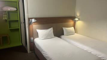 A hotel room with two single beds, a green wardrobe, and a small stool.