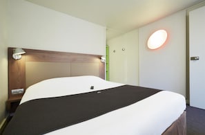 Una cama bien hecha con colcha blanca y negra, un cabecero de madera y lámparas de noche.