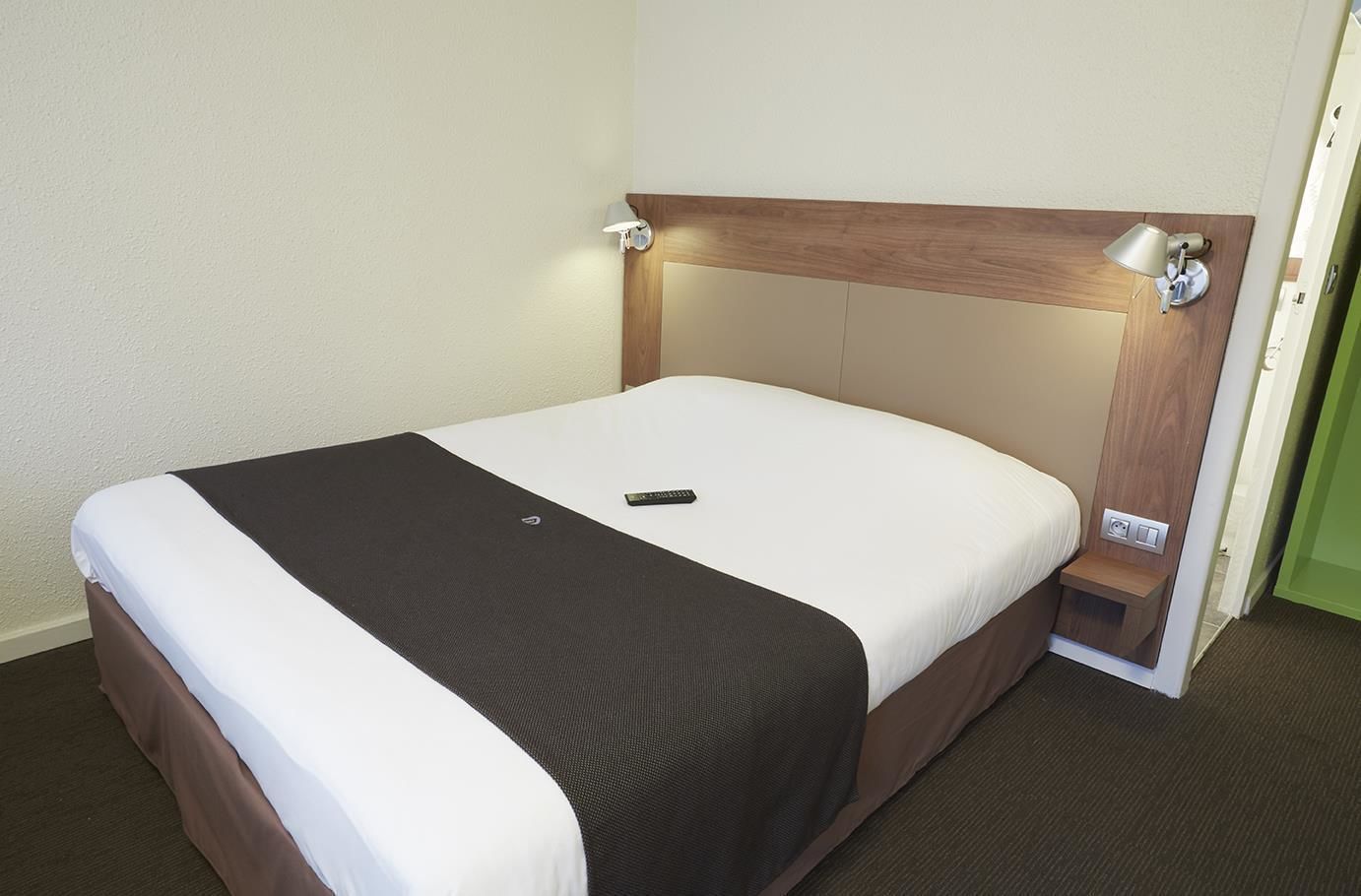Una cama bien hecha con un control remoto encima, un cabecero de madera y lámparas de noche.